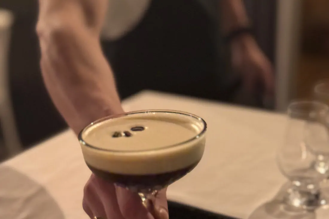 Close-up of an espresso martini served in a coupe, three coffee beans resting on the foam, in warm low light