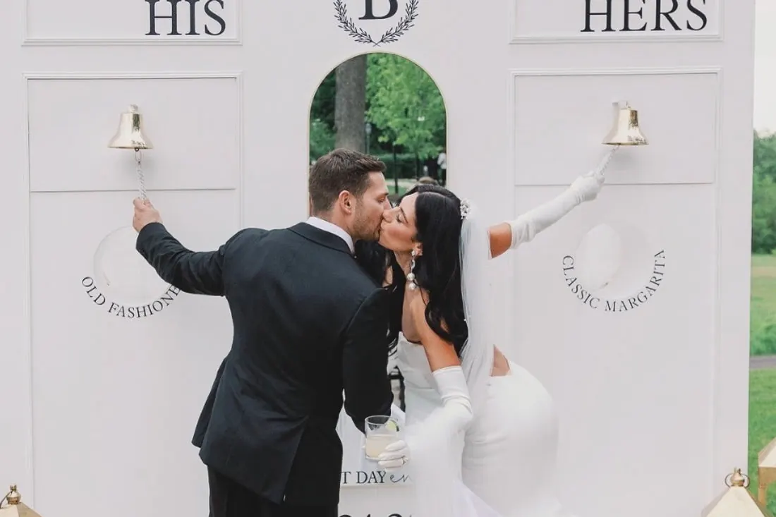 A bride and groom kissing between His and Hers cocktail walls, each ringing the bell for an Old Fashioned and a Classic Margarita